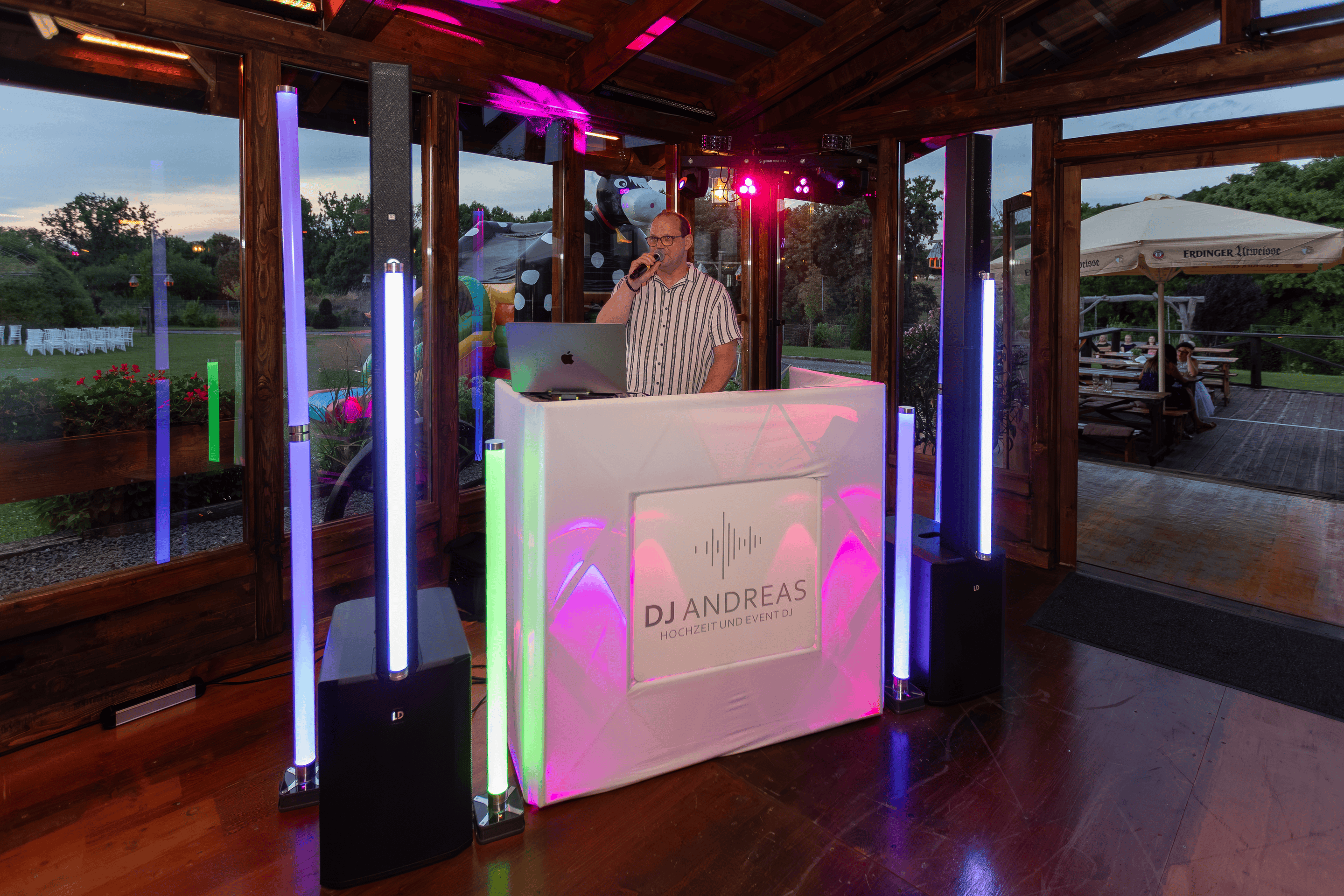 DJ Andreas moderiert eine Freie Trauung – modernes DJ-Setup mit LED-Lichttechnik in einer hellen Eventlocation mit offenem Blick nach draußen.