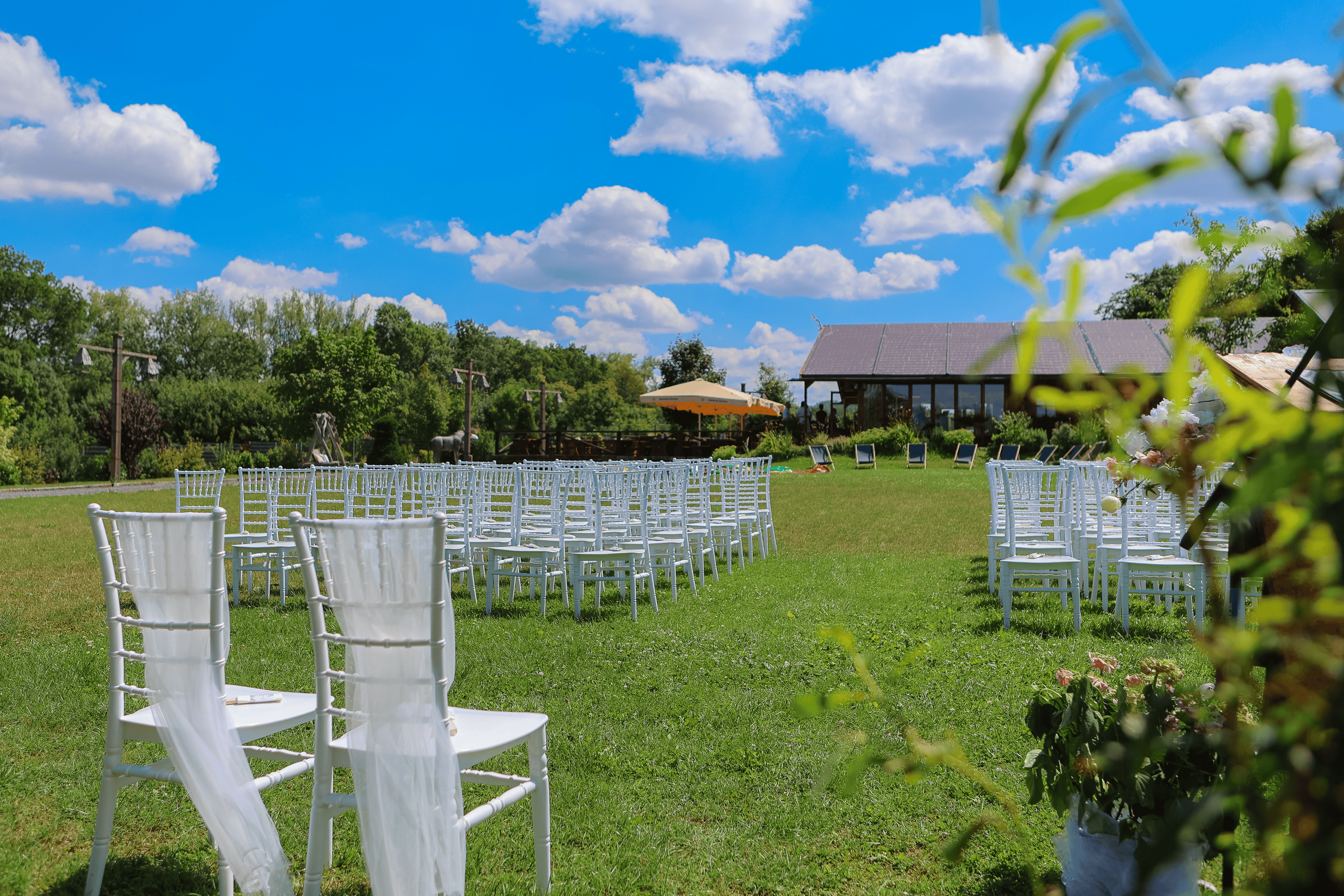 Aufgebauter Sitzbereich für eine Freie Trauung im Grünen – weiße Stühle auf einer Wiese mit Blick auf die Feierlocation unter blauem Himmel.